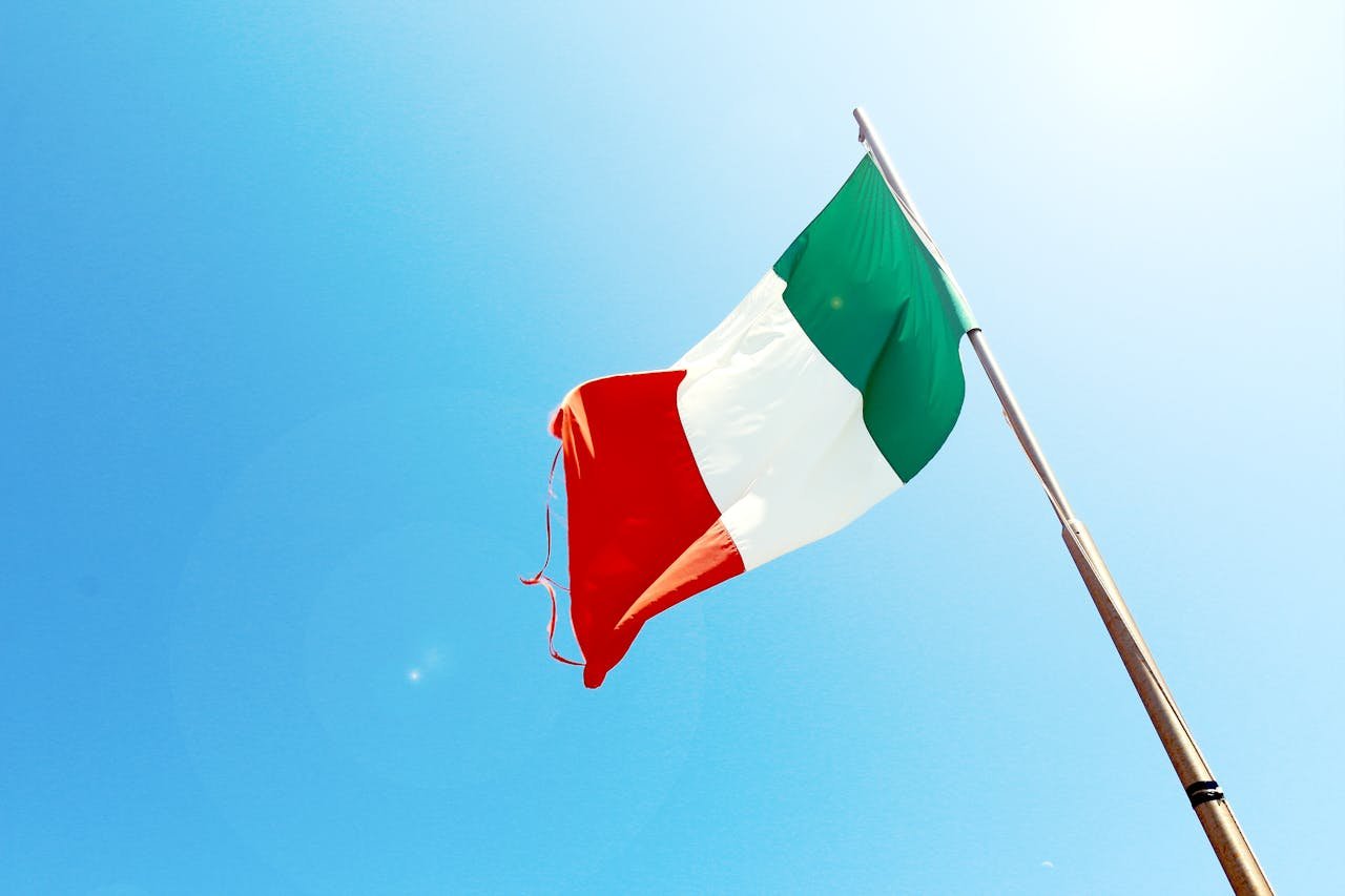 awards-img Vivid image of the Italian flag waving on a flagpole against a bright blue sky.
